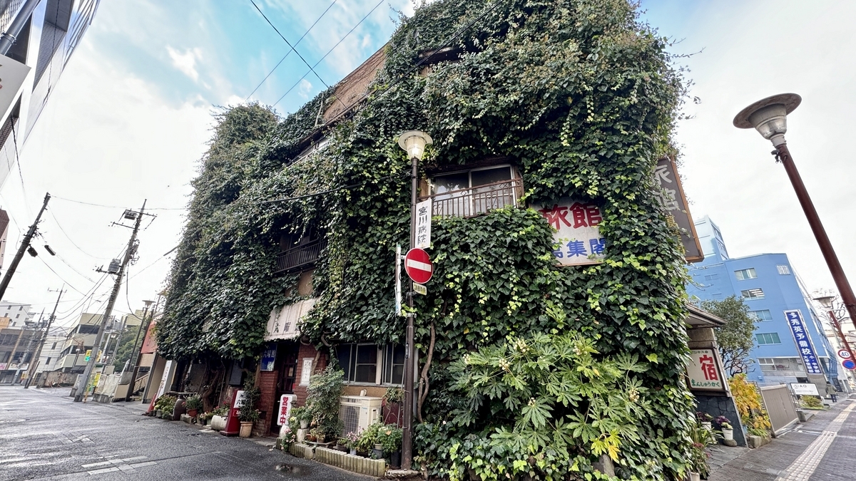 담쟁이로 뒤덮인 로쿠요칸 건물 외관과 모퉁이의 숙소 간판이 서 있는 골목