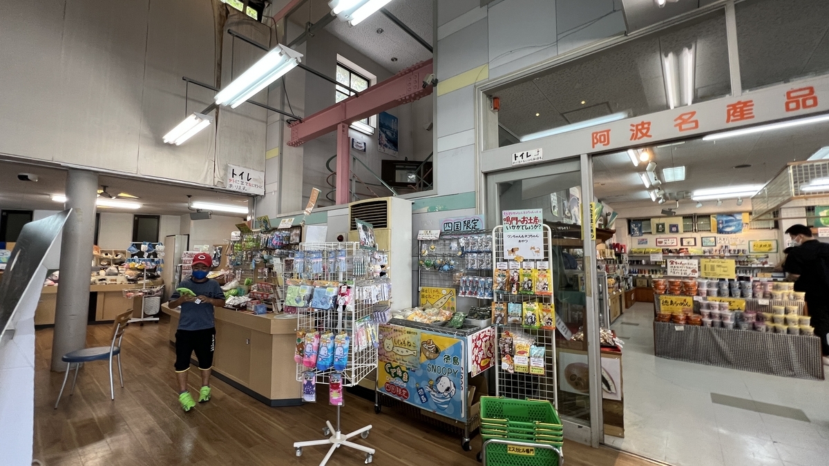 บริเวณทางเข้าร้านของฝากที่เต็มไปด้วยขนมและเครื่องดื่ม นักท่องเที่ยวพร้อมเด็กกำลังเลือกซื้อสินค้า