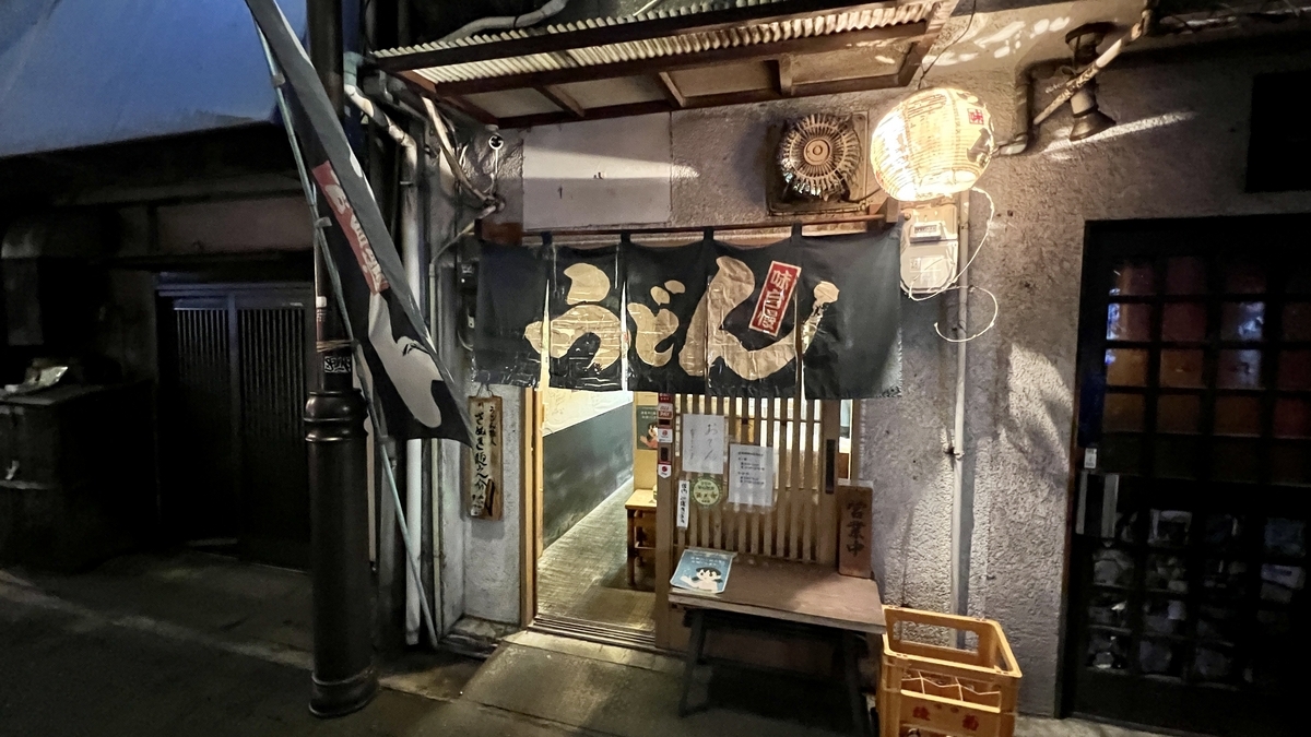 夜のさぬき麺之介の店舗外観。暖簾が下がる入口と木のベンチが置かれた路地沿いの様子