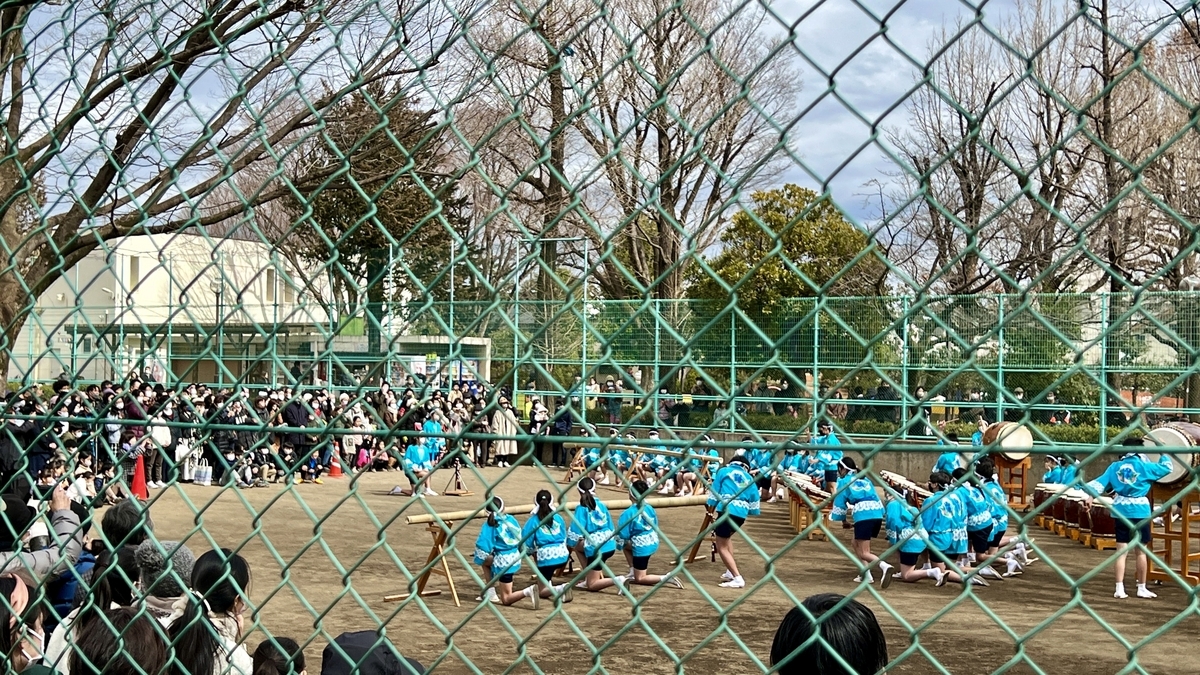 Children in blue festival coats striking taiko drums in unison