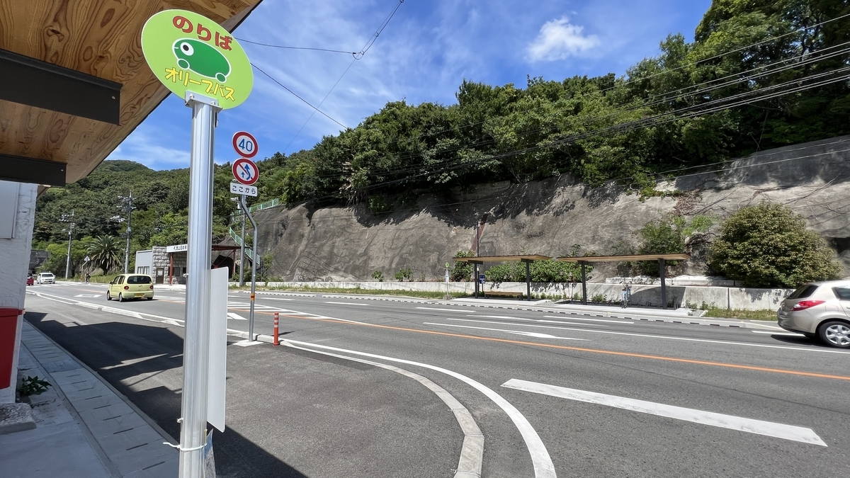 Kusakabe Port bus stop with a road and mountain backdrop.