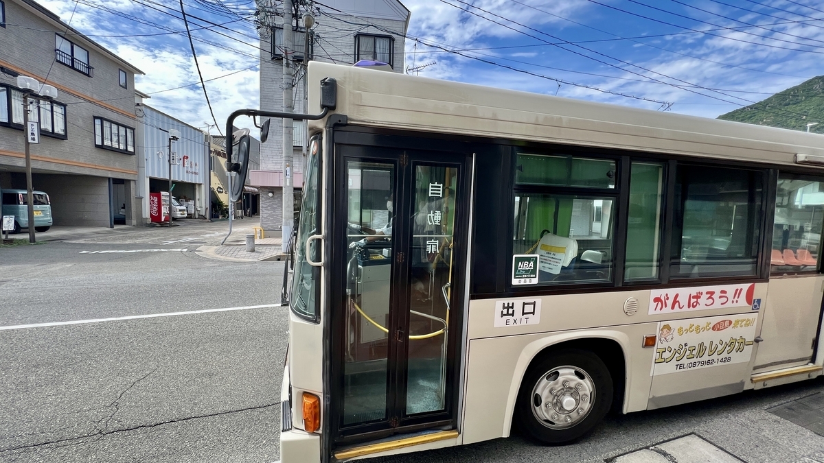 Bus stopped in front of a shopping street at Tonosho Honmachi with surrounding buildings.