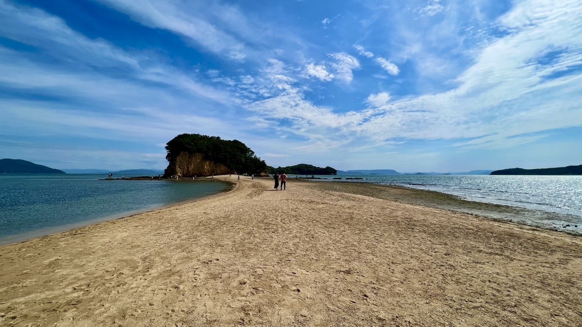 Sandbar revealed during low tide, leading to a small island under a blue sky.