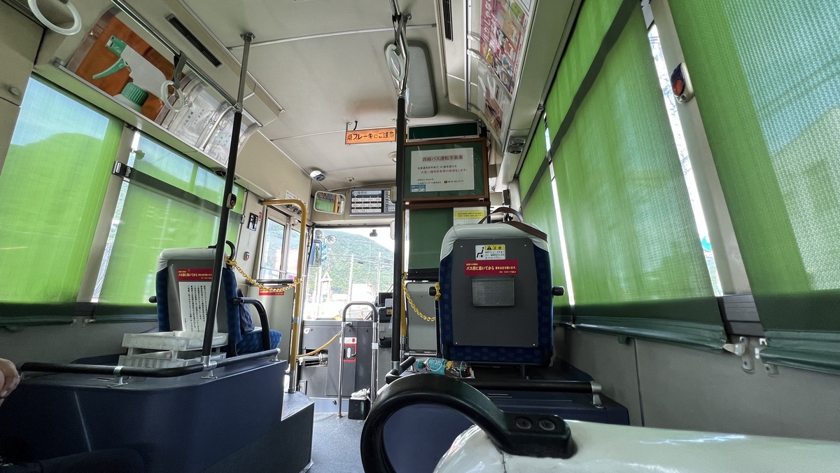 Bus interior with sunlight filtered through green curtains and outside view.