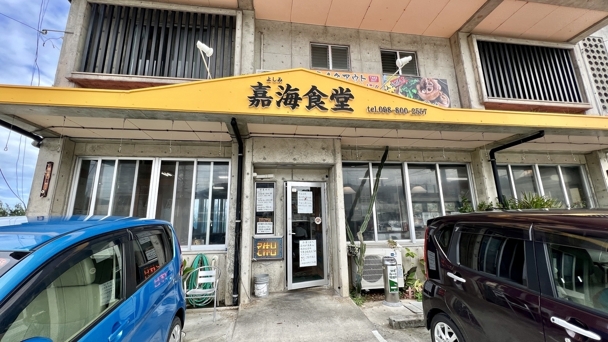 Exterior of Yoshimi Shokudo in Kin Town with a yellow signboard and cars parked in front