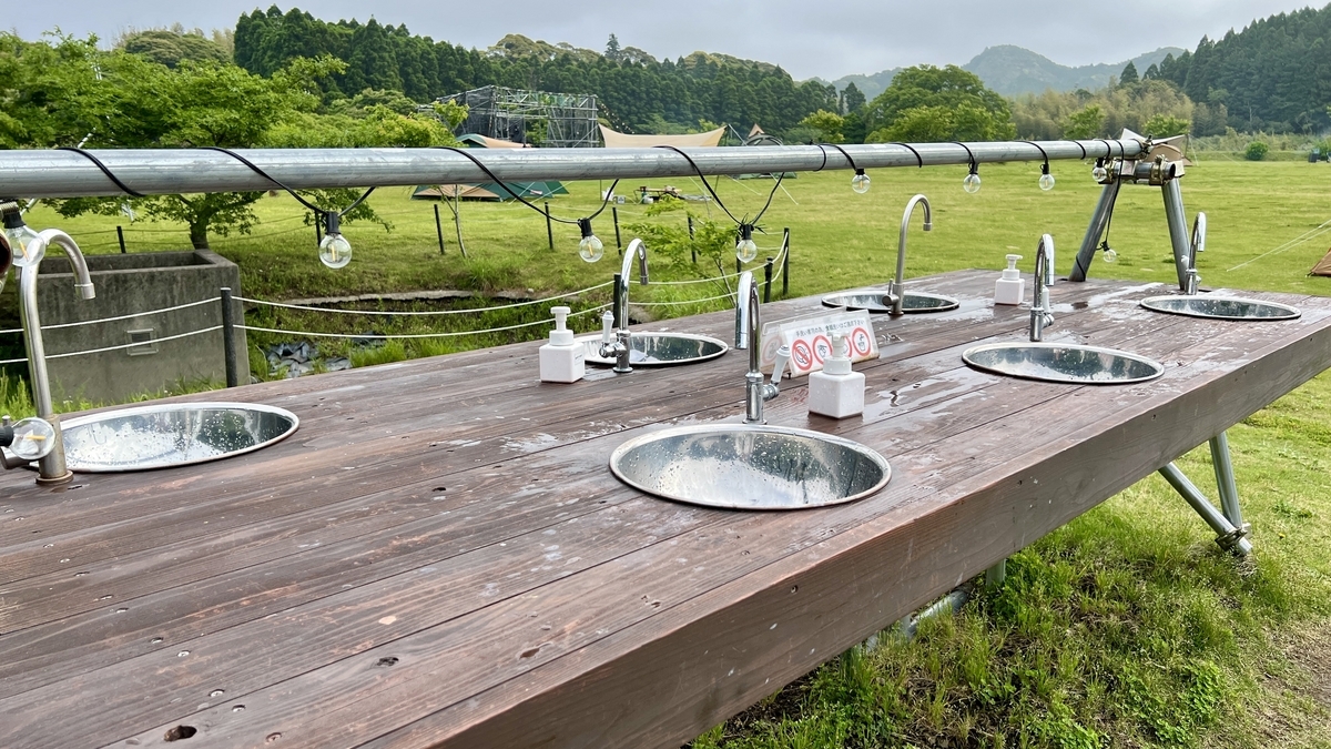 木製のカウンターにシンクが並ぶ屋外洗面場と広がる芝生の風景
