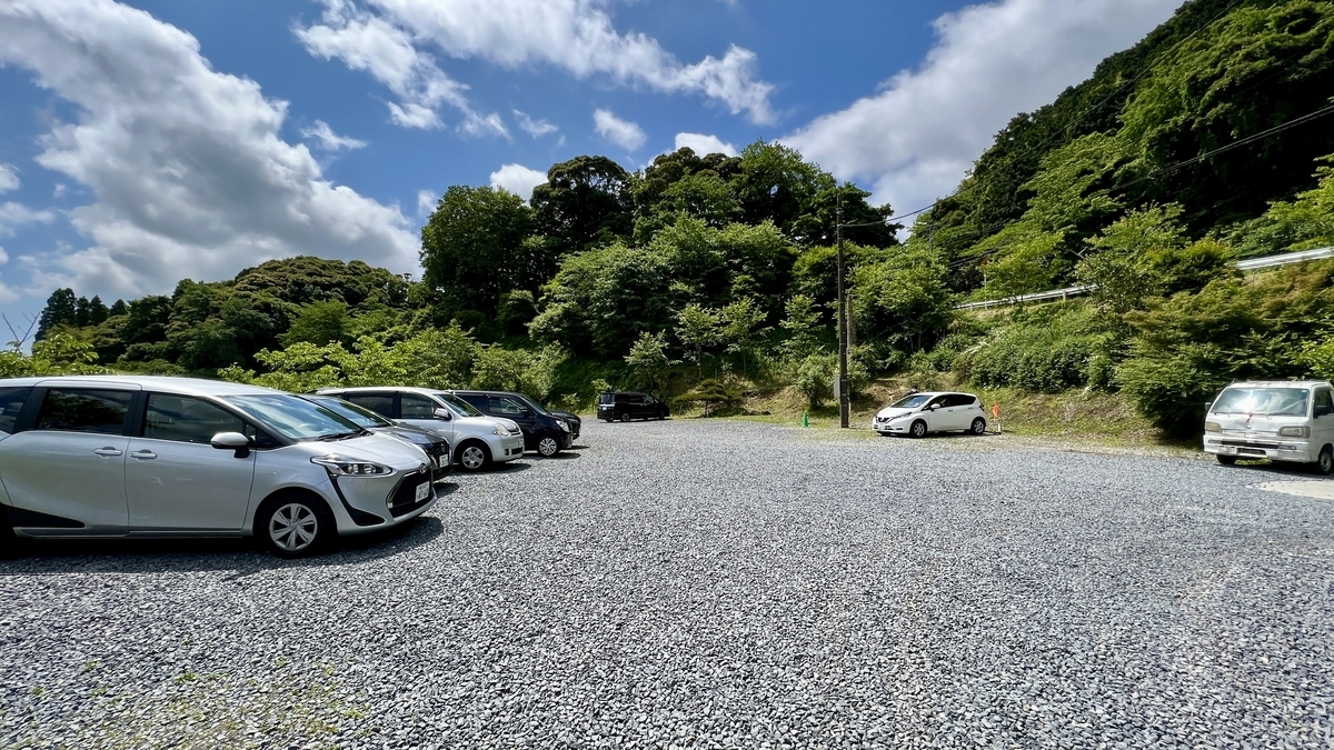 木々に囲まれた砂利敷きの広い駐車場と停車中の車