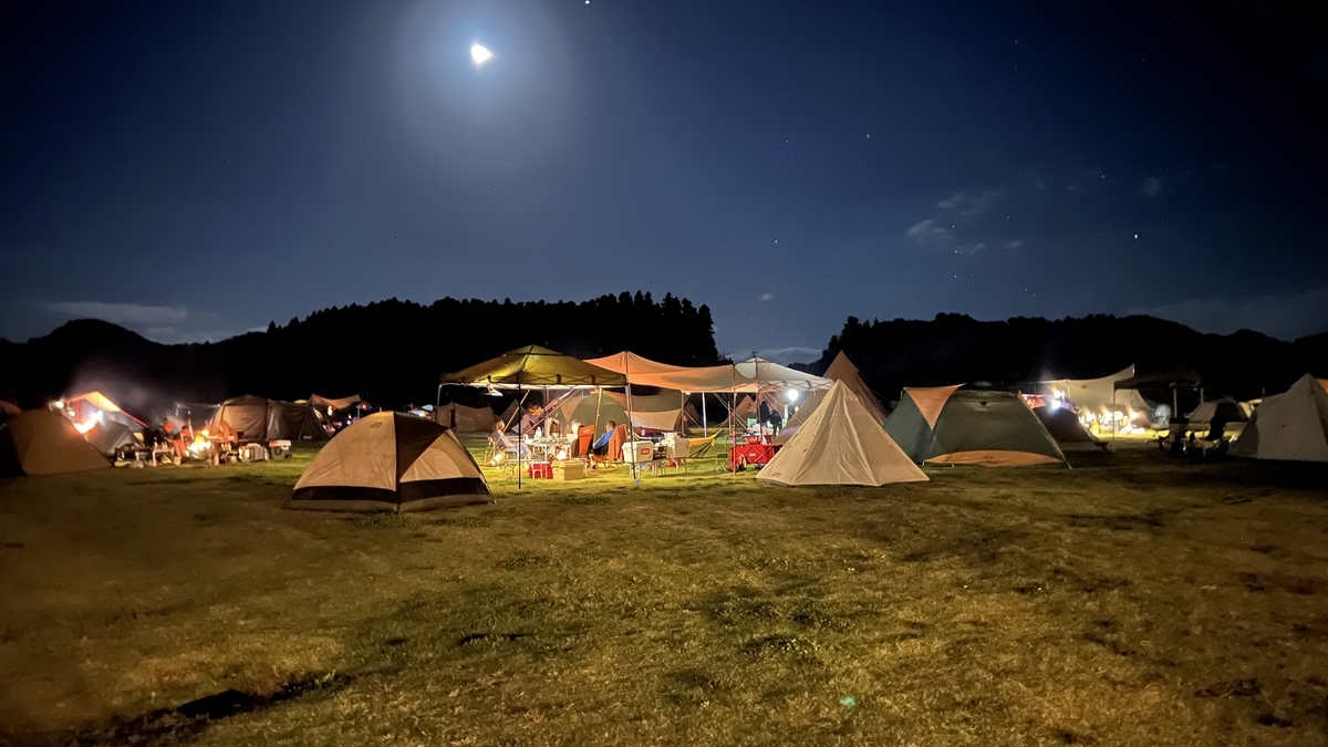 夜空の下でテントの明かりが灯る広々としたキャンプサイトの風景