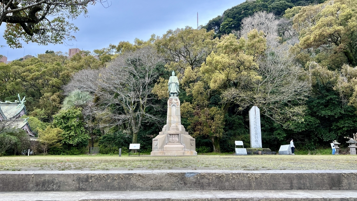 รูปปั้นท่านลอร์ดชิมาสึ นาริอากิระตัดกับท้องฟ้าสีฟ้าและต้นไม้สีเขียว