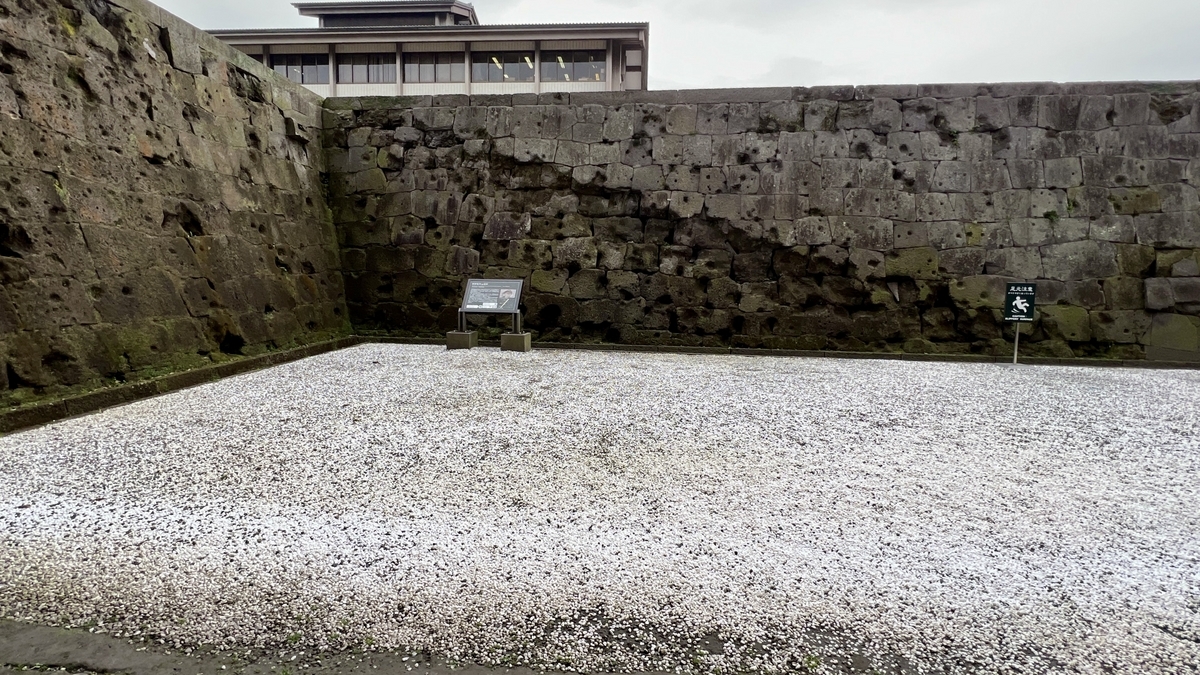 Historic site with stone walls scarred by Seinan War bullets and an explanatory signboard nearby