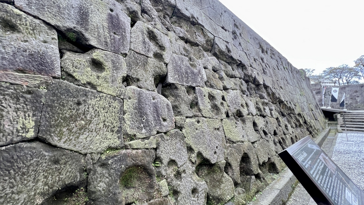 Oblique angle view showing dense clusters of bullet scars across the stone wall