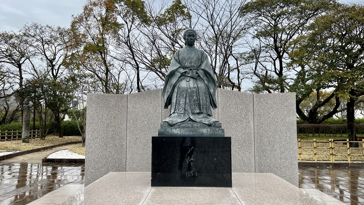 Statue of Tenshōin Atsuhime standing on its pedestal surrounded by trees in the Reimeikan plaza