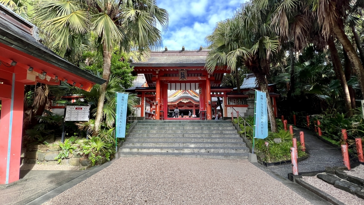 熱帯植物に囲まれた参道の先に朱色の門が見える南国風の青島神社の風景