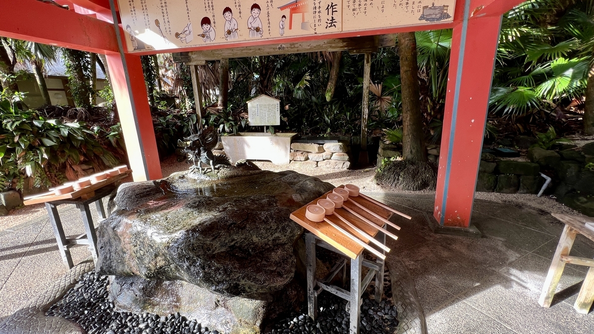 石の水盤と柄杓が置かれた青島神社の手水舎 熱帯植物に囲まれた清め場