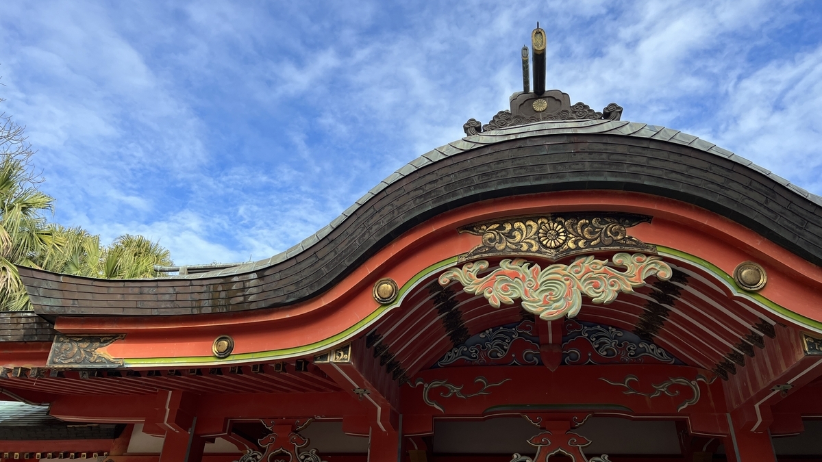 青島神社拝殿の屋根と彫刻を見上げた写真 青空の下で朱色と金色の装飾が際立つ