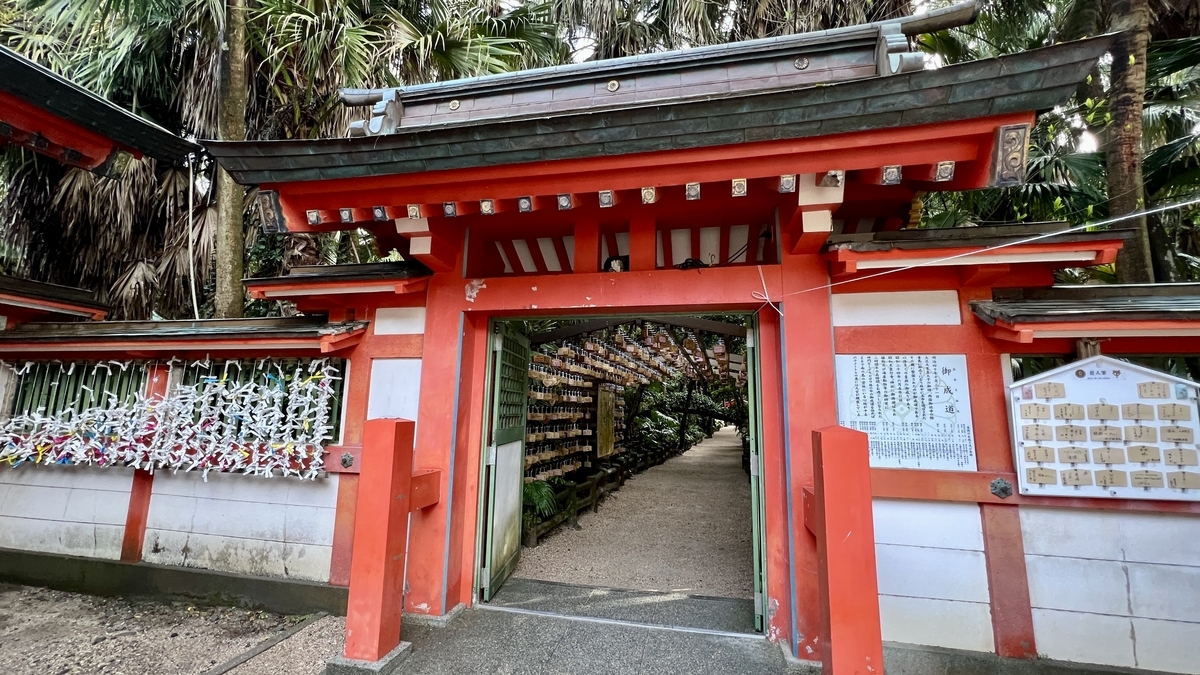 赤い門の奥に絵馬が連なる祈りの古道の入口 周囲に緑が生い茂る参道の風景