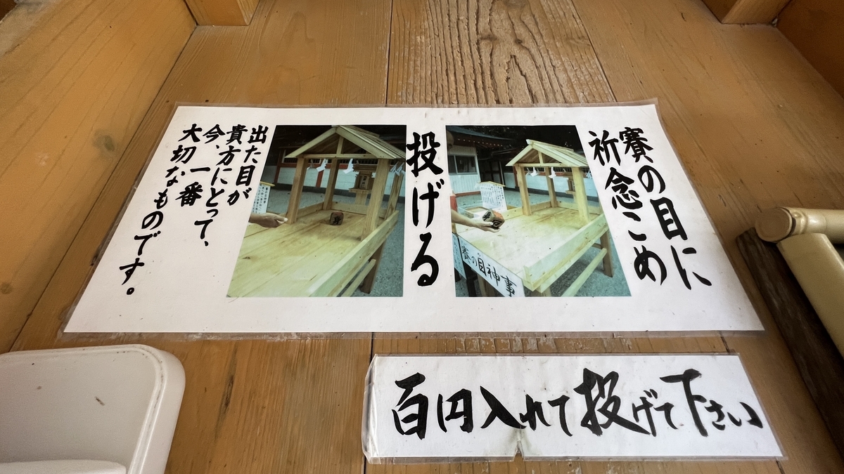 賽の目神事の手順が書かれた案内板と台の様子 投じ方と意味を示す説明が並ぶ