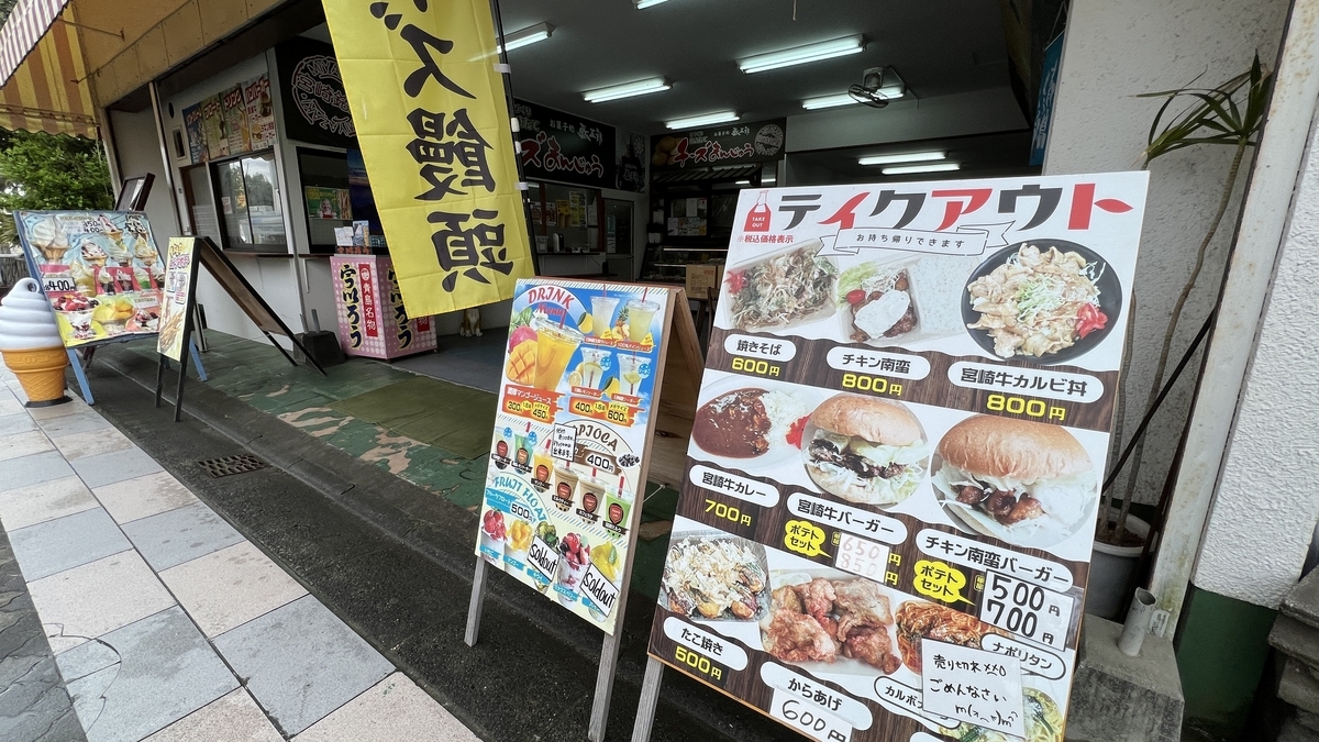 青島参道商店街の店舗前に並ぶテイクアウトメニューの看板と食品の写真が描かれた大きなパネル