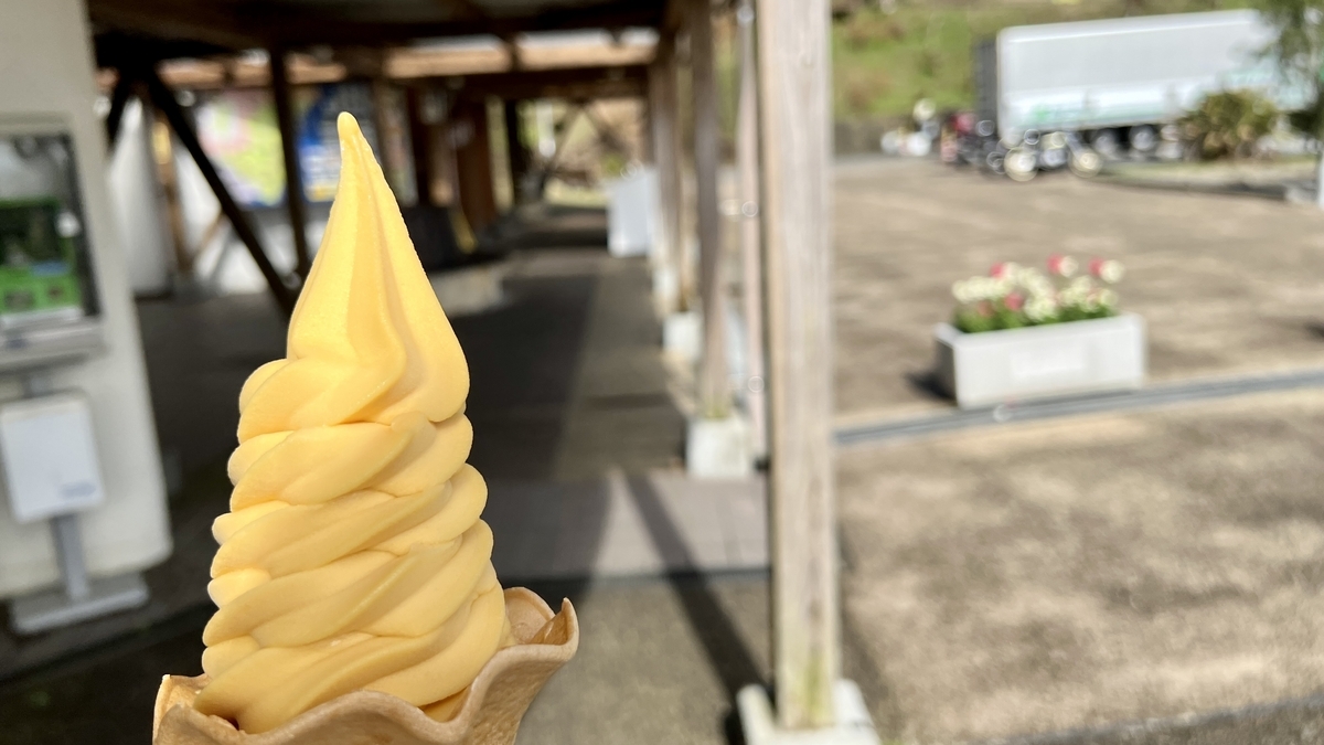 マンゴーソフトクリームを手に持ち青空と海を背景にした爽やかな景色