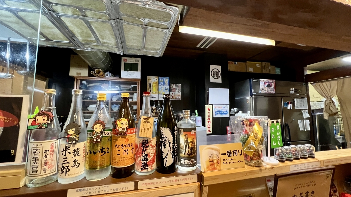 Interior con botellas de sake alineadas en la barra y la cocina visible al fondo