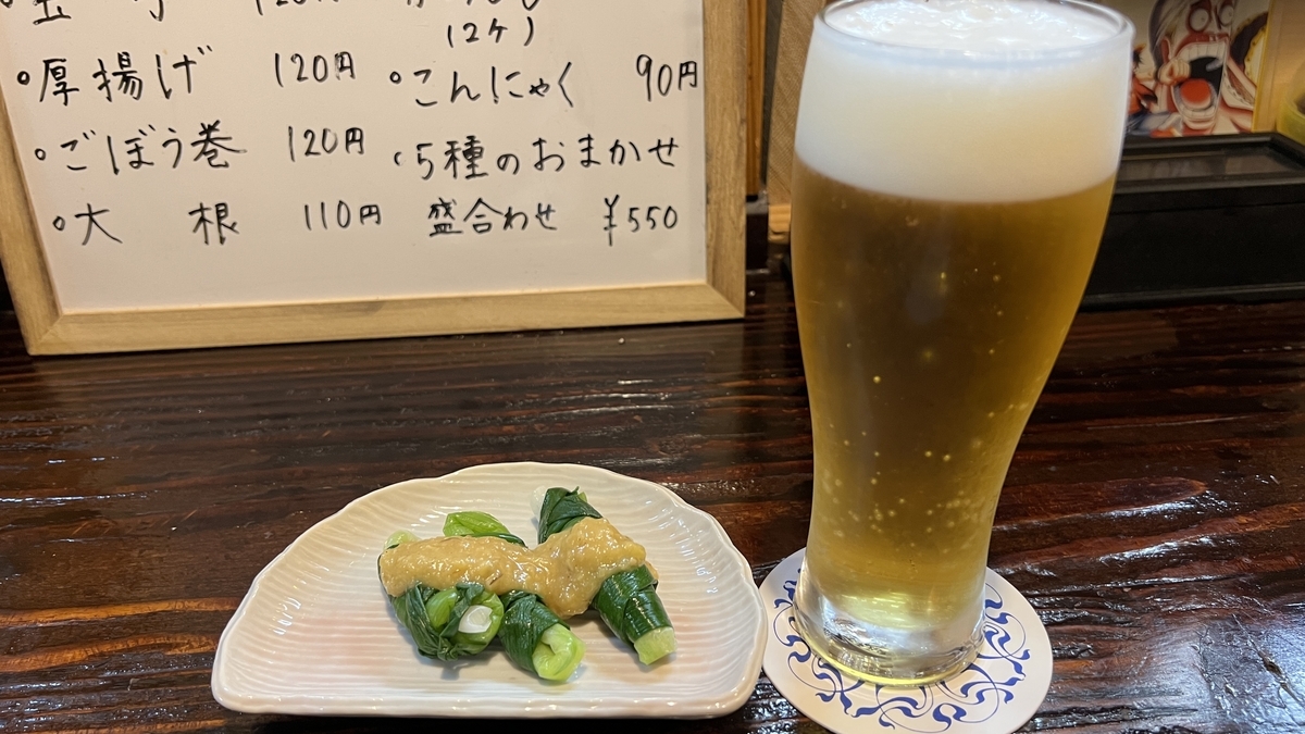Cerveza de barril espumosa junto a un pequeño plato de verduras con salsa de miso