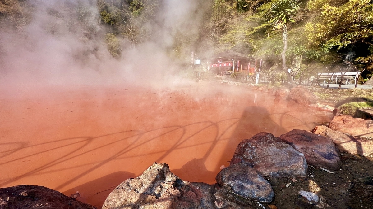 Vista de la piscina roja humeante con tienda de regalos visible al fondo en Chinoike Jigoku