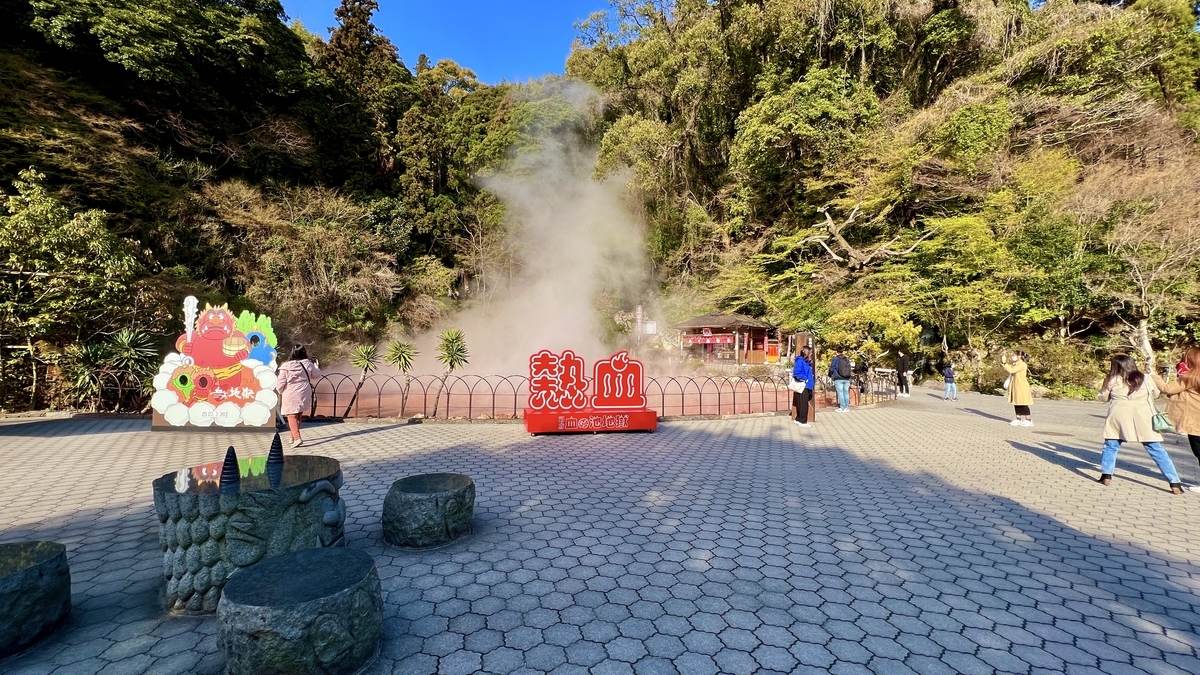 Plaza que rodea la piscina roja con monumento Nekketsu y paneles de oni en Chinoike Jigoku