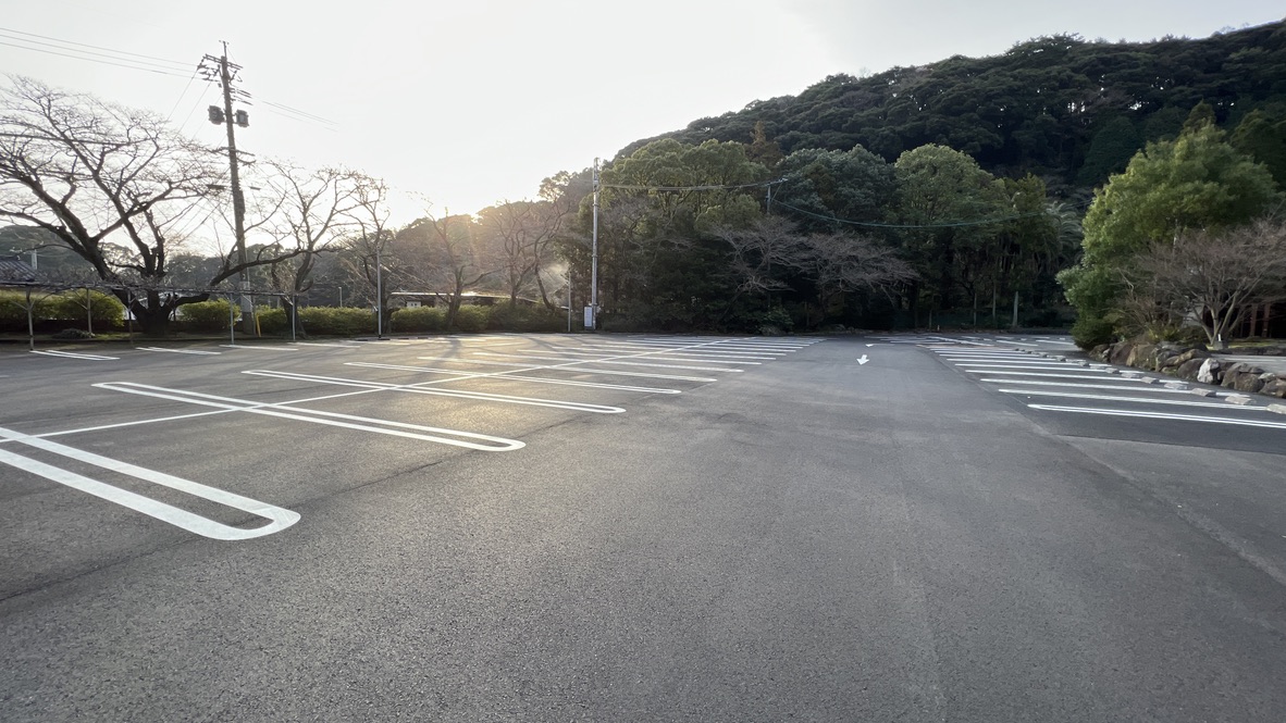 Amplio estacionamiento con líneas blancas bajo la luz del atardecer con bosque y colinas al fondo
