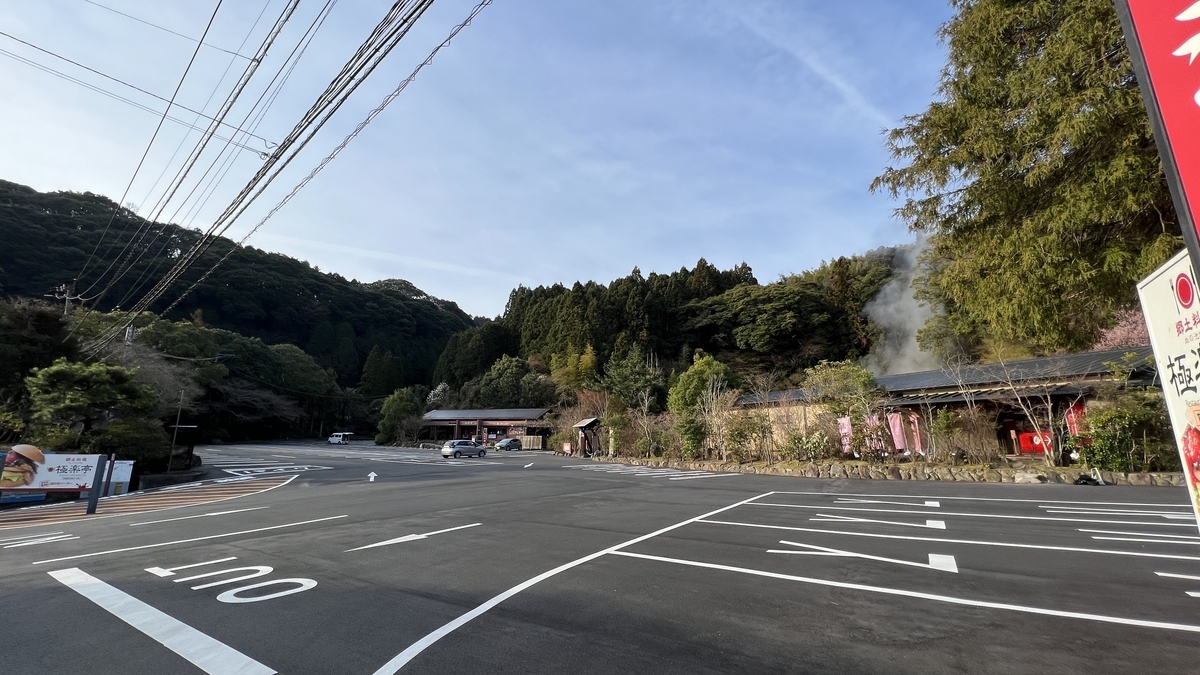 Amplio estacionamiento con edificios de Chinoike Jigoku y vapor ascendiendo visibles al fondo