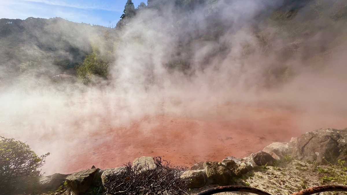 Vapor ascendiendo de la piscina roja con rocas alineando el borde en Chinoike Jigoku