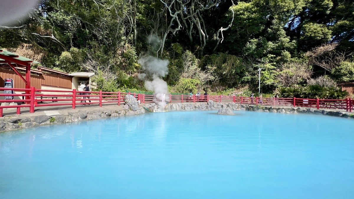 빨간 울타리로 둘러싸인 파란 온천 수면과 증기, 뒤편의 숲
