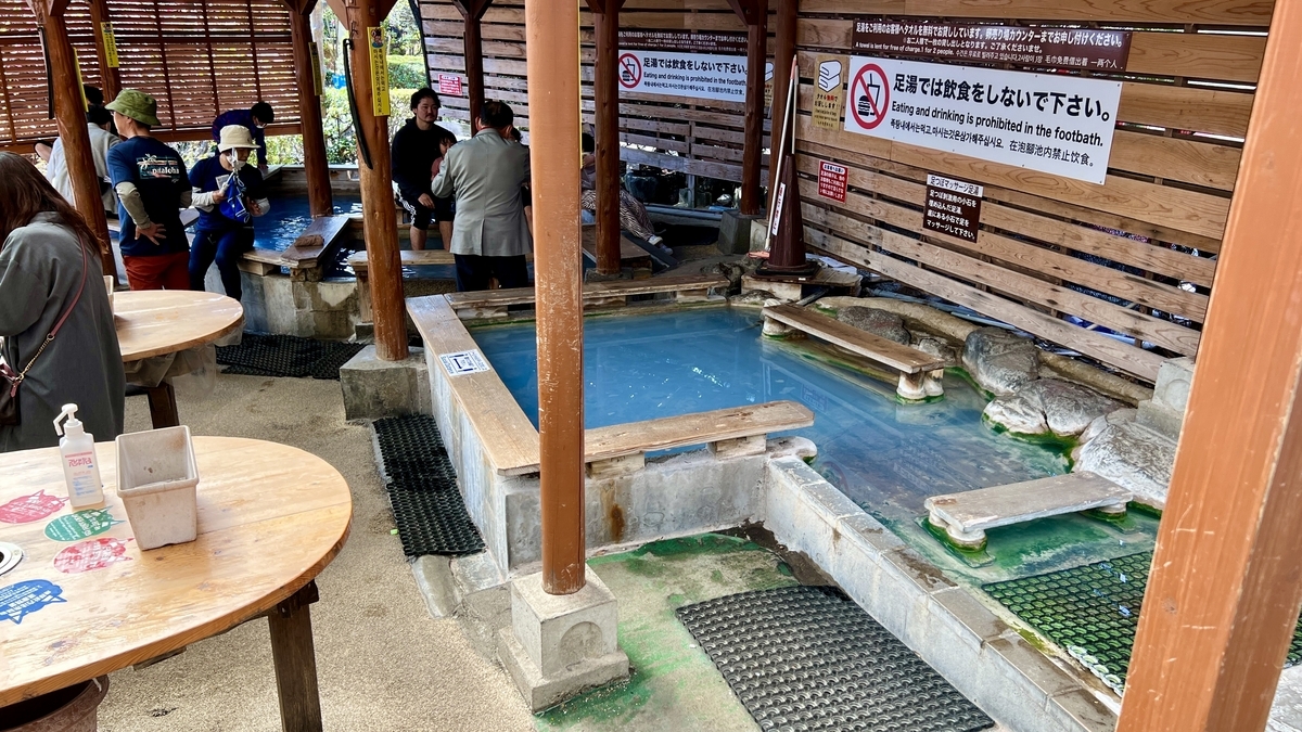 파란 물이 가득 찬 지붕 있는 족욕탕에 앉아 쉬는 사람들