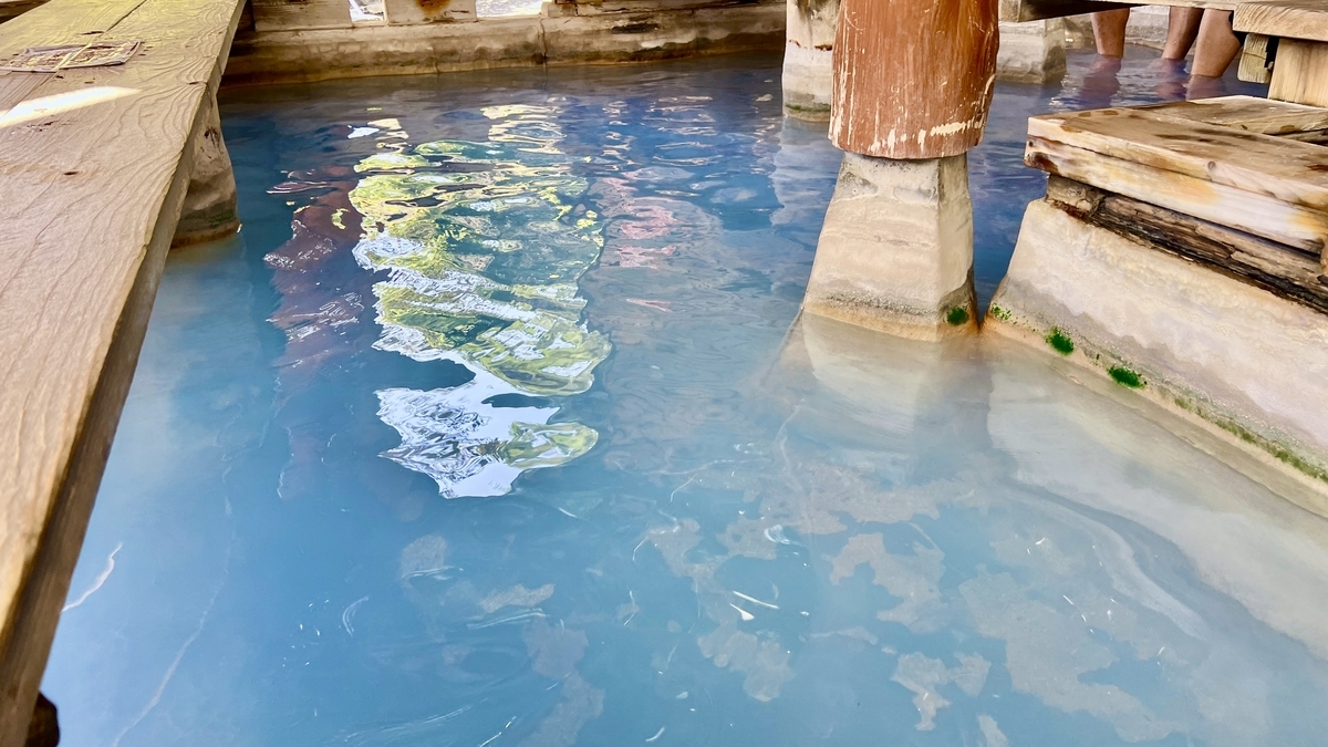 파란 족욕탕 수면에 비친 나무 기둥과 벤치
