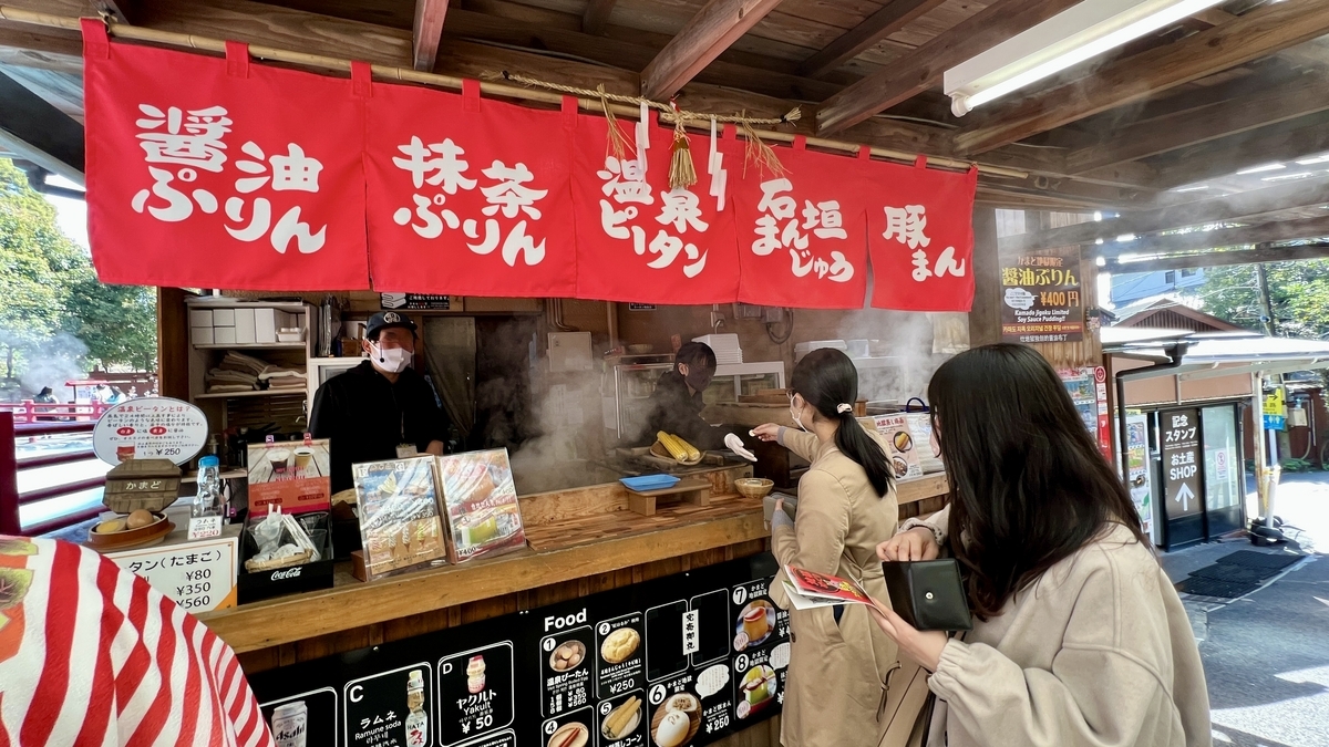 빨간 노렌이 걸린 지옥 스위츠 매점에서 푸딩과 온천 달걀을 주문하는 손님들