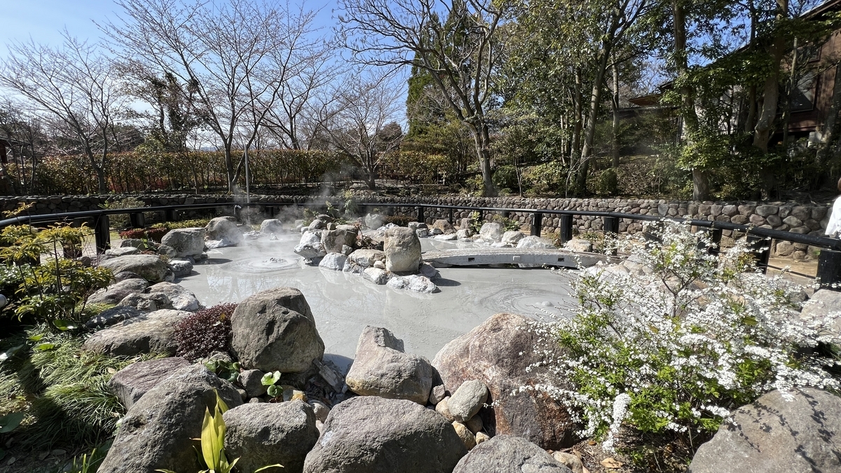 Vista completa del estanque de barro blanco caliente integrándose con las rocas del jardín en Oniishi Bouzu Jigoku