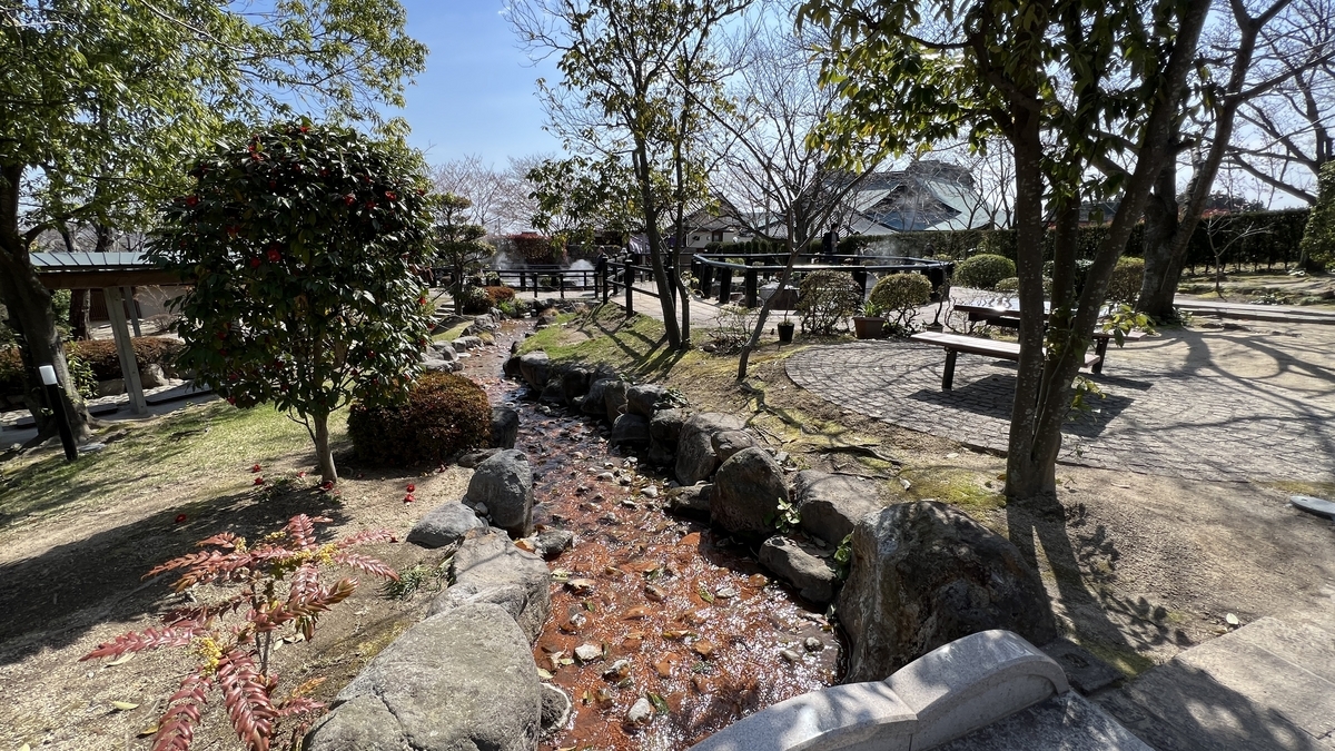 Arroyo de aguas termales de color marrón rojizo fluyendo por el jardín con bancos