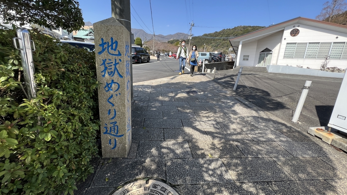 地獄めぐり通りの石柱が立つ歩道で観光客が歩き車道と建物が並ぶ風景