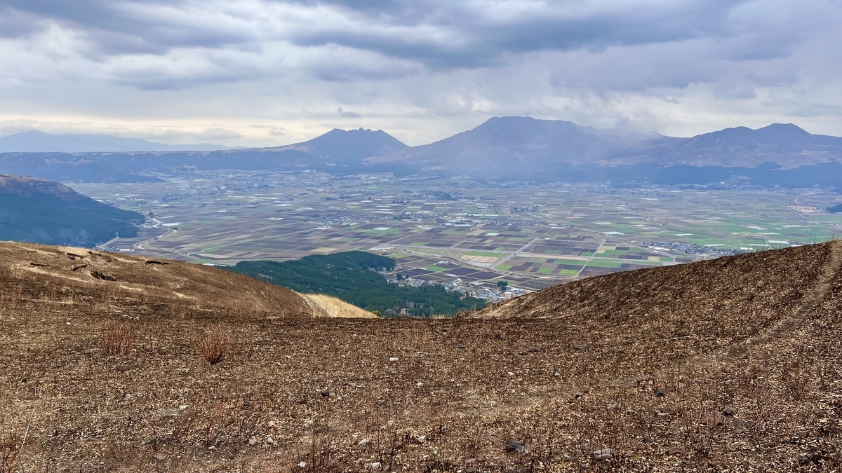透过烧焦的山坡眺望阿苏火山口底的农田与阿苏五岳