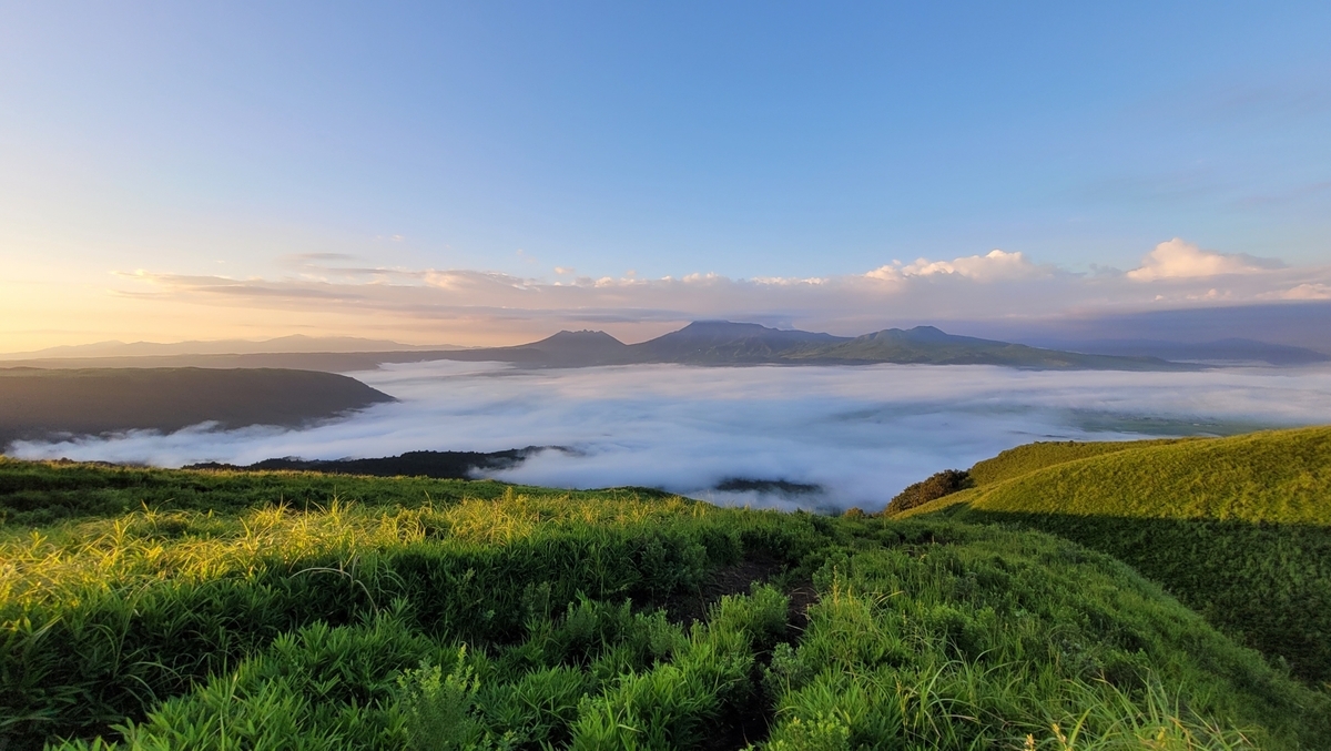 晨光照射的草原斜坡与漂浮在云海中的阿苏火山口