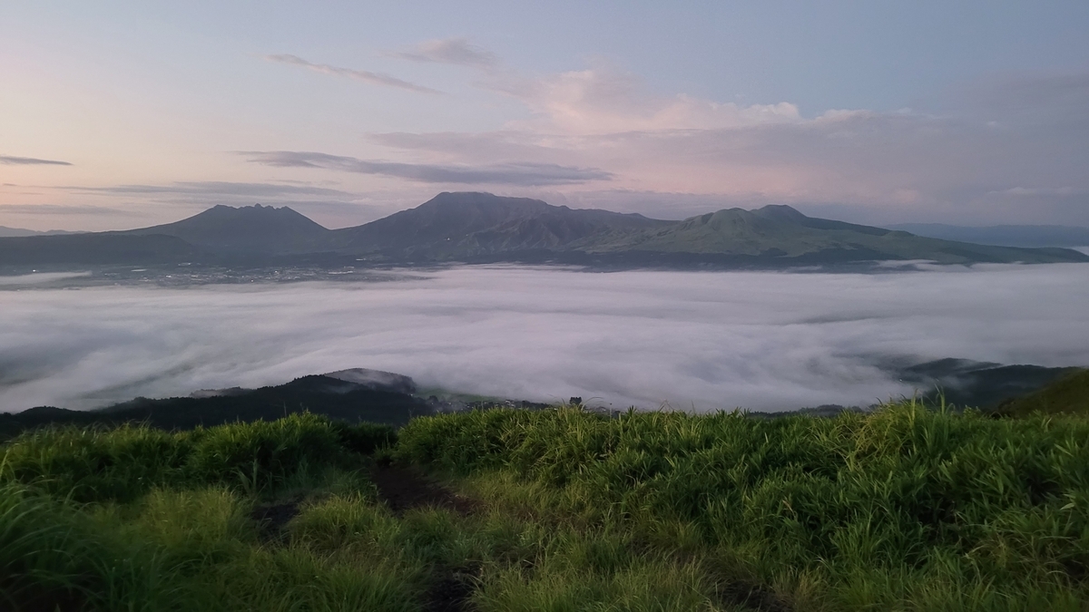 黎明天空中阿苏五岳漂浮在云海上与前方的草原