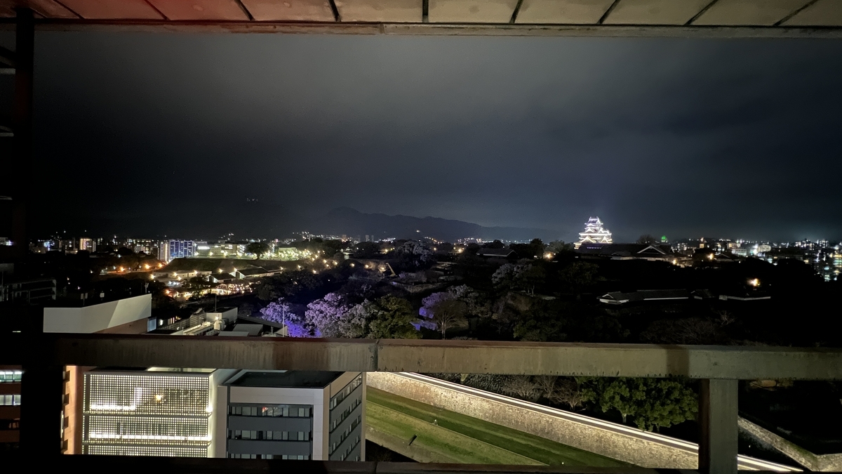 透过观景大厅窗框看到的熊本城天守阁和沿石垣的步道夜景