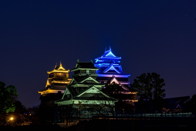 被蓝色和金色灯光照亮的熊本城天守阁和橹并排的夜景