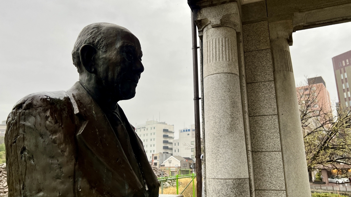 沾着雨滴的高桥守雄胸像侧面与门廊遗构石柱并列