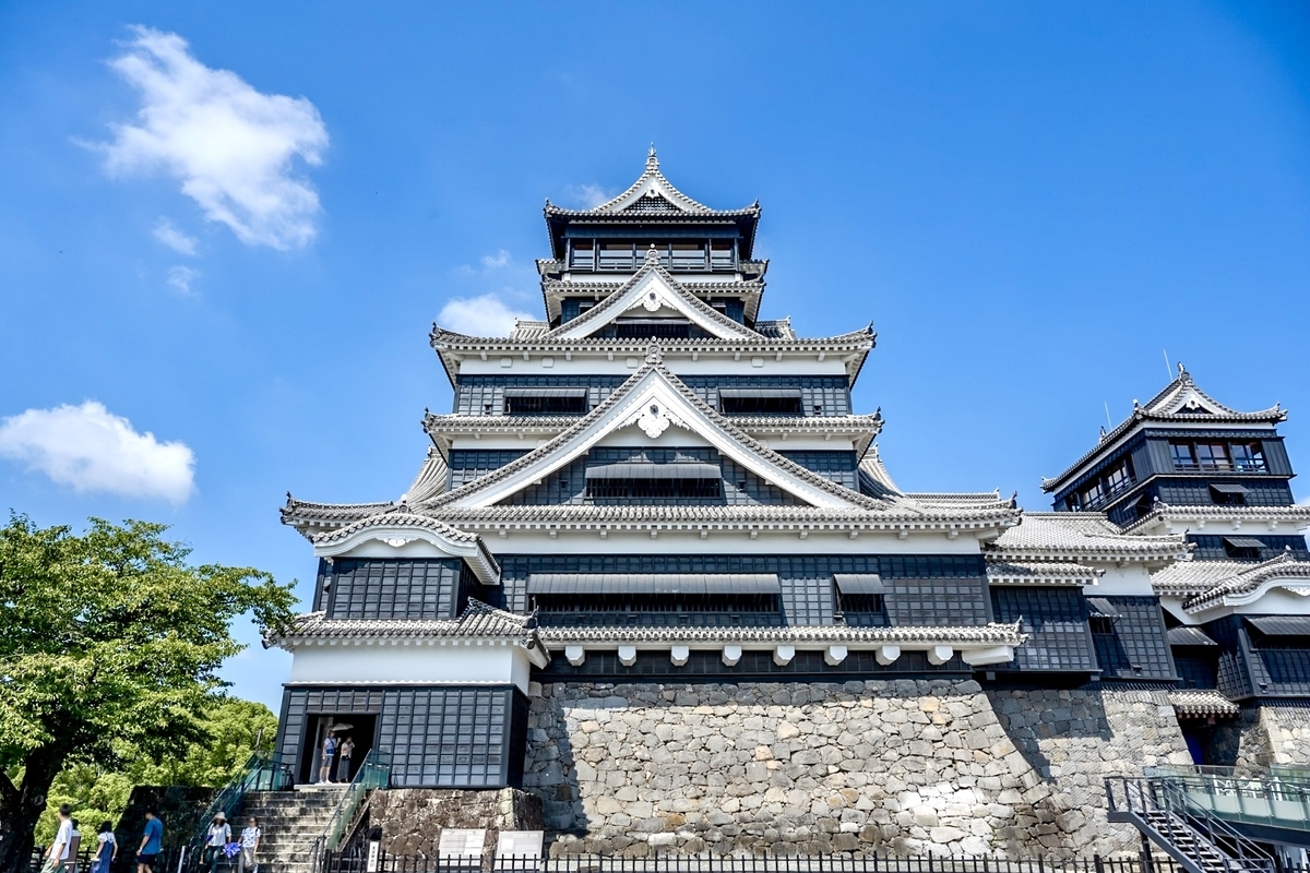 푸른 하늘 아래 우뚝 솟은 구마모토성 천수각의 검은색과 흰색 외관과 석축