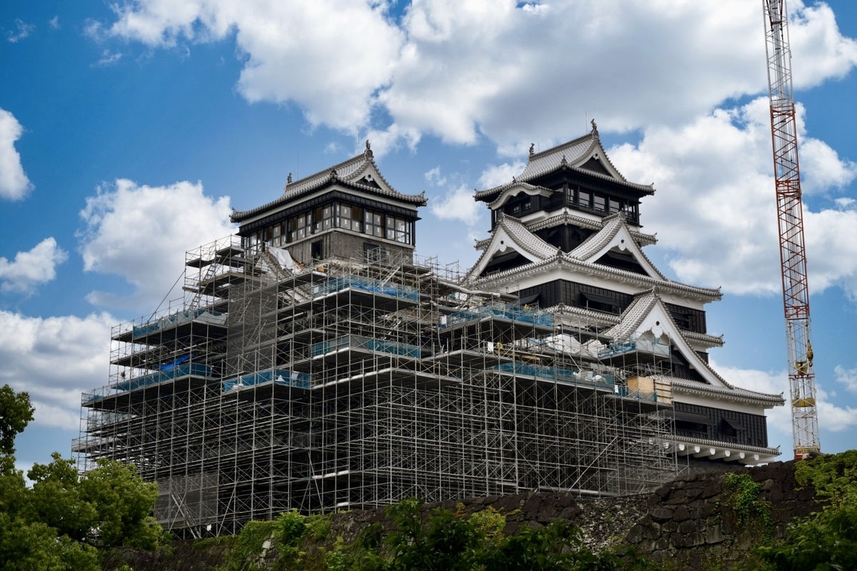 비계로 덮여 복구 공사가 진행 중인 구마모토성 천수각과 푸른 하늘로 뻗은 크레인