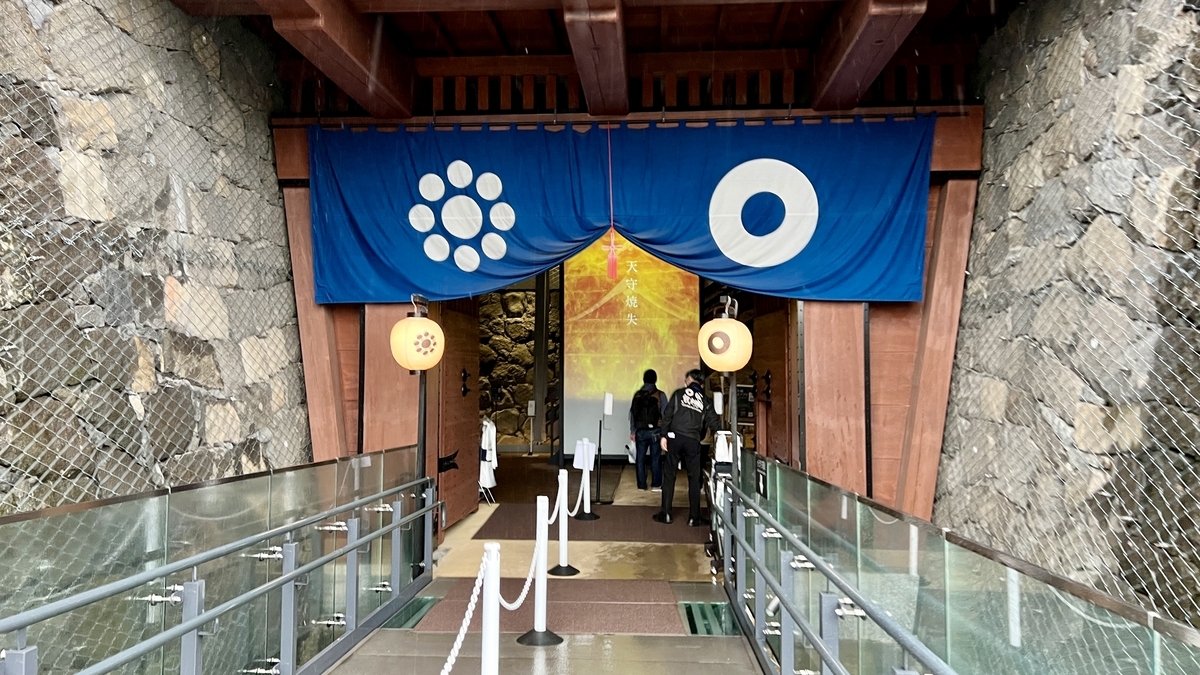 파란 막과 제등이 걸린 구마모토성 천수각 입구의 목조 문과 석축 통로