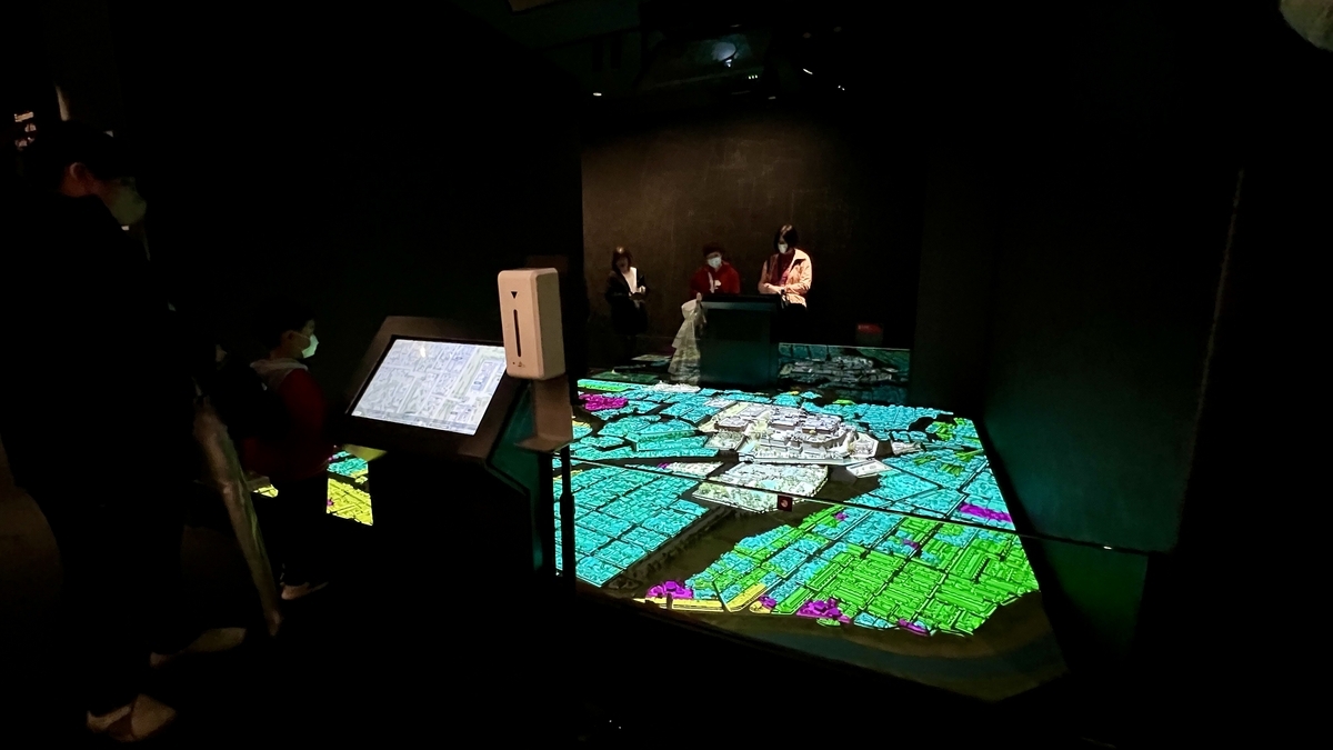 성하마을 모형에 선명한 색의 투사를 겹친 프로젝션 매핑 전시를 둘러싼 방문객들