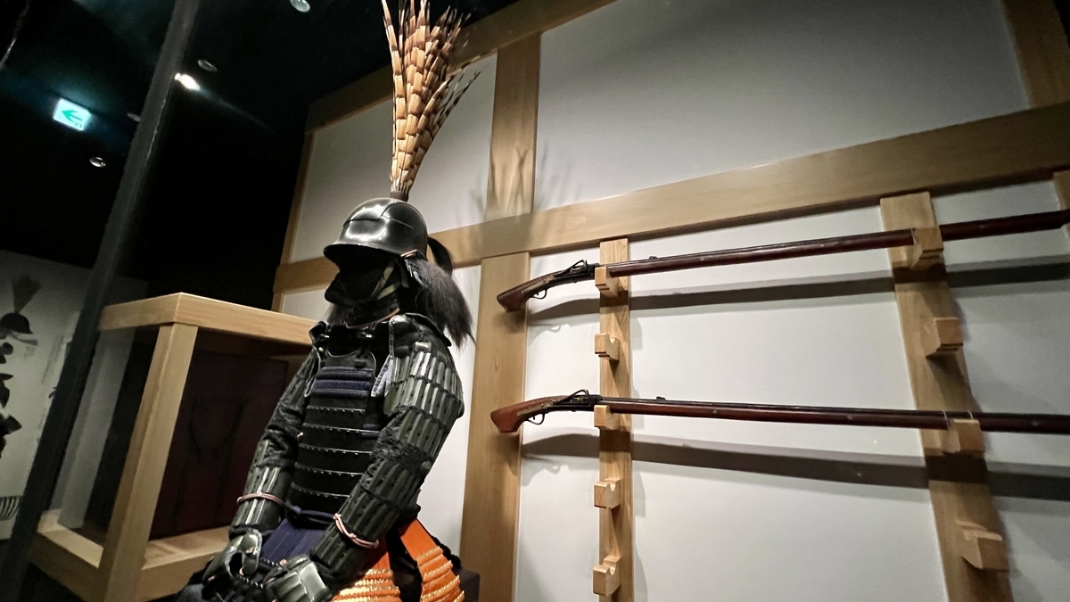 검은 갑옷과 긴 투구 장식이 서 있는 전시와 벽에 늘어선 화승총