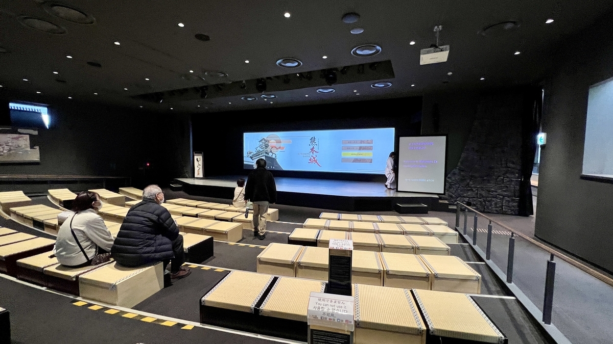 구마모토성 영상을 상영하는 와쿠와쿠자 극장과 다다미 좌석에 앉은 관람객