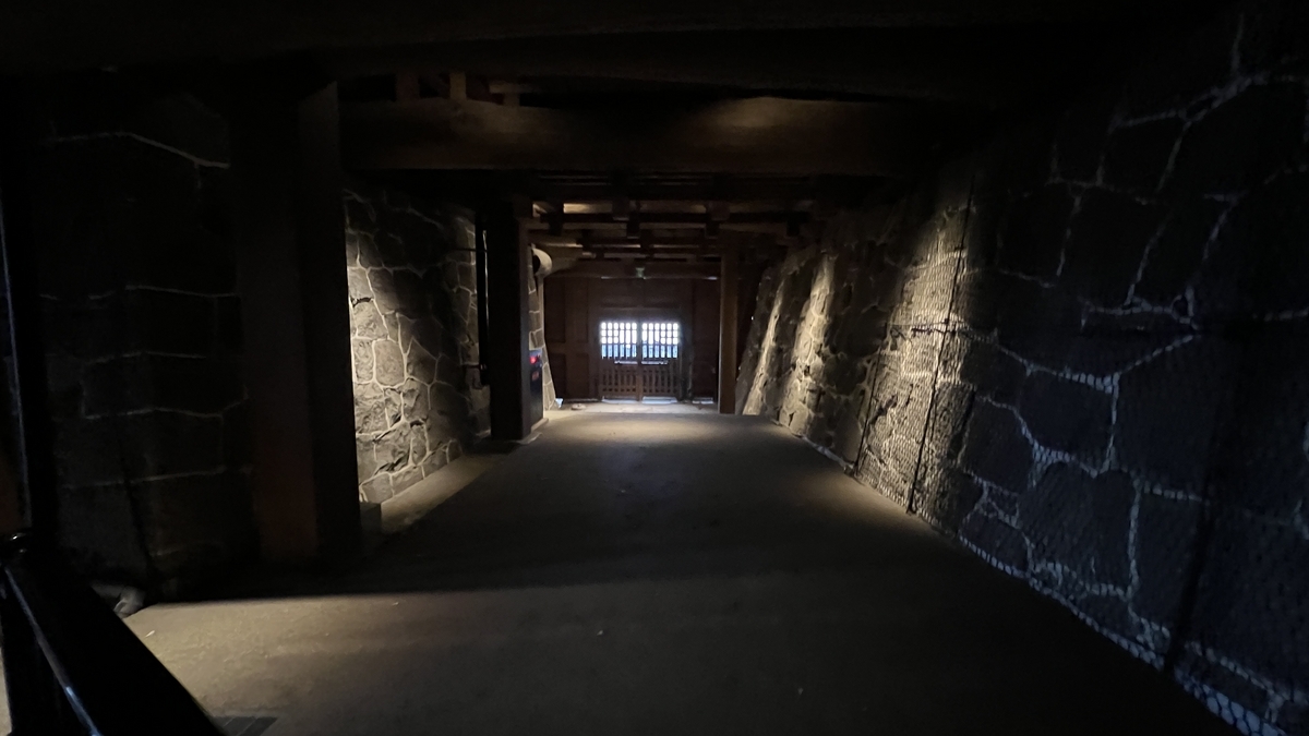 희미한 구마모토성 지하 통로의 석축 벽과 멀리 보이는 나무 격자 출구